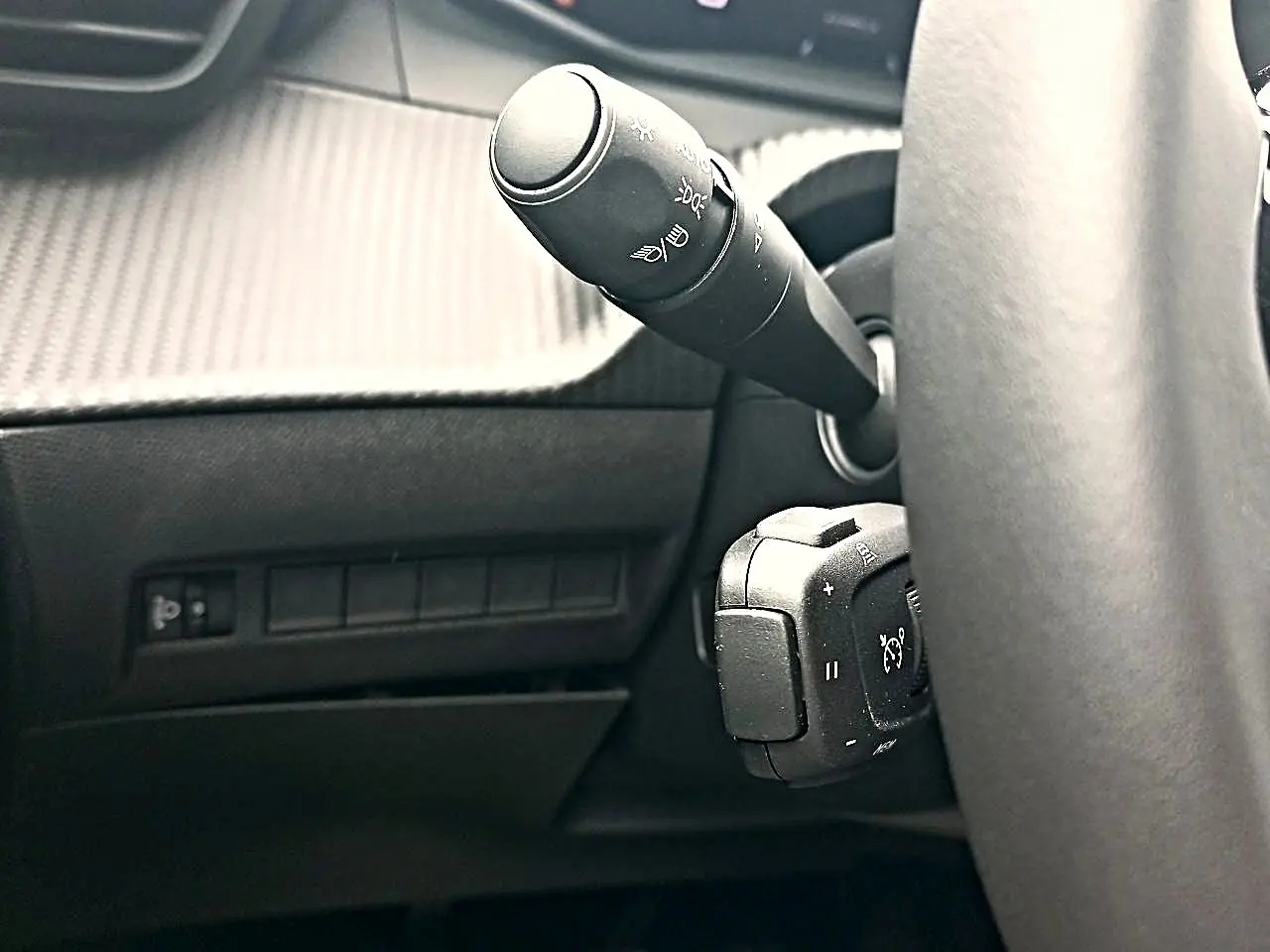 Gros plan sur la manette de commandes au volant côté gauche dans l'habitacle sombre du Peugeot 2008 rouge Elixir.