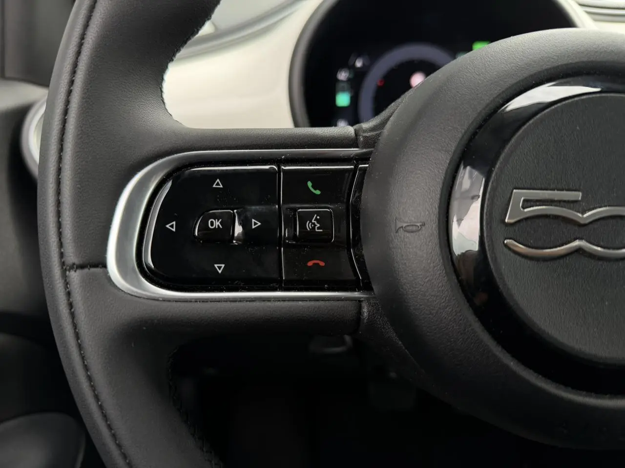 Gros plan sur le volant noir Soft-Touch de la Fiat 500 électrique 2024 avec commandes intégrées et logo 500 central.