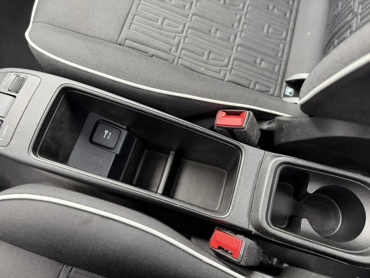 Vue rapprochée de la console centrale et des sièges tissu noir avec surpiqûres blanches de la FIAT 500 électrique 2024.