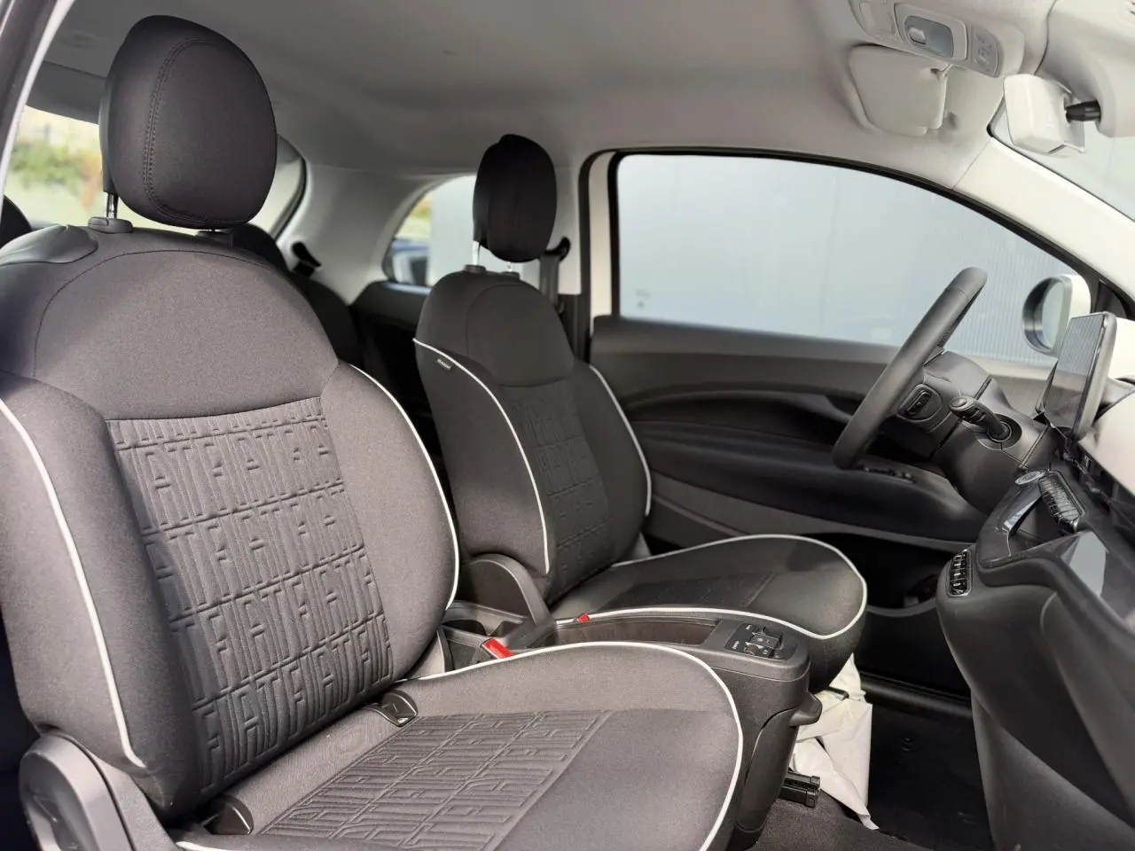 Vue intérieure côté droit montrant les sièges avant noirs avec surpiqûres blanches et planche de bord noire de la Fiat 500 électrique.
