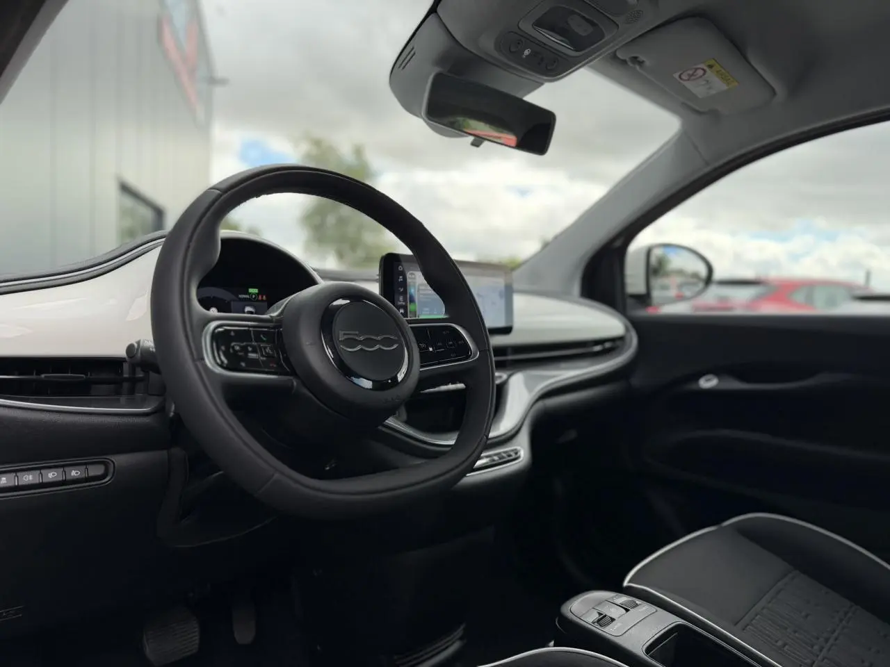 Vue intérieure côté conducteur de la Fiat 500 électrique 2024 avec tableau de bord blanc Artic et volant noir Soft-Touch.