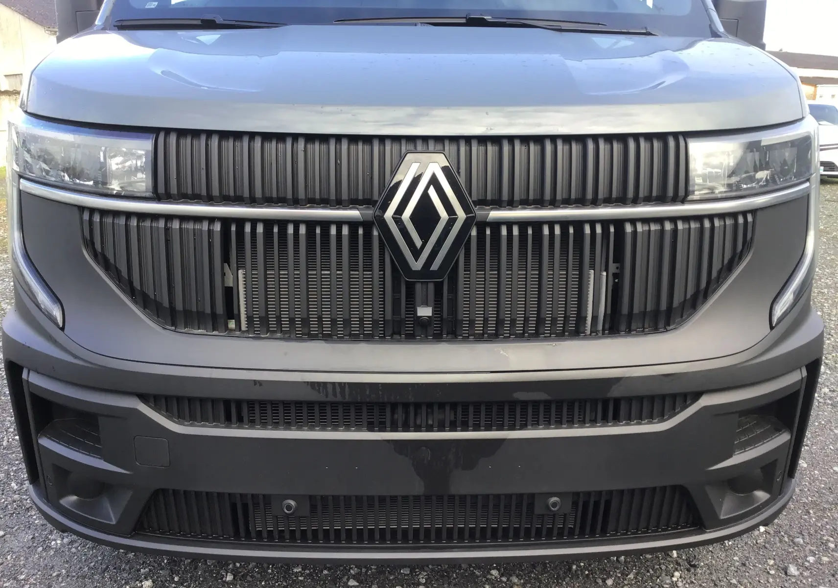 Vue frontale rapprochée du Renault Master gris urbain 2025 avec calandre noire et logo central proéminent.