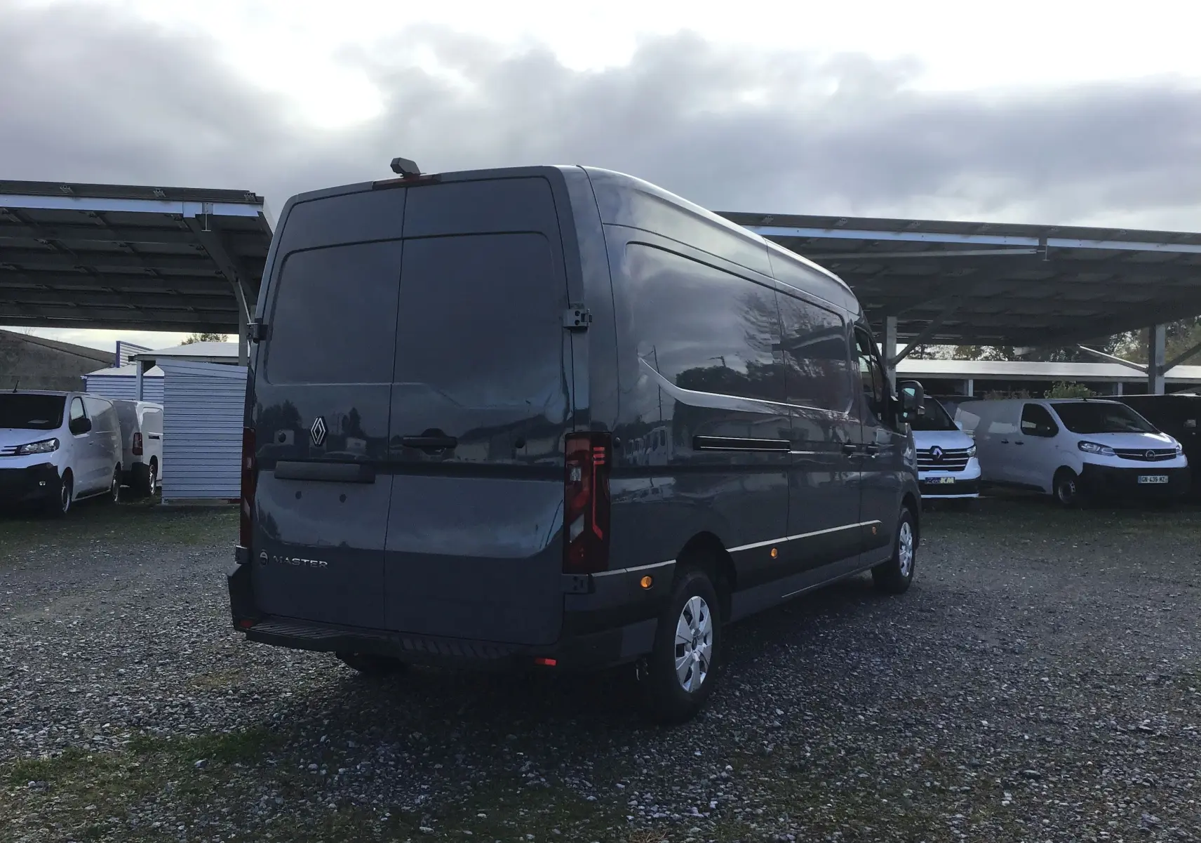 Renault Master gris urbain vu en 3/4 arrière droit, avec porte arrière fermée et marchepied sous le pare-chocs.