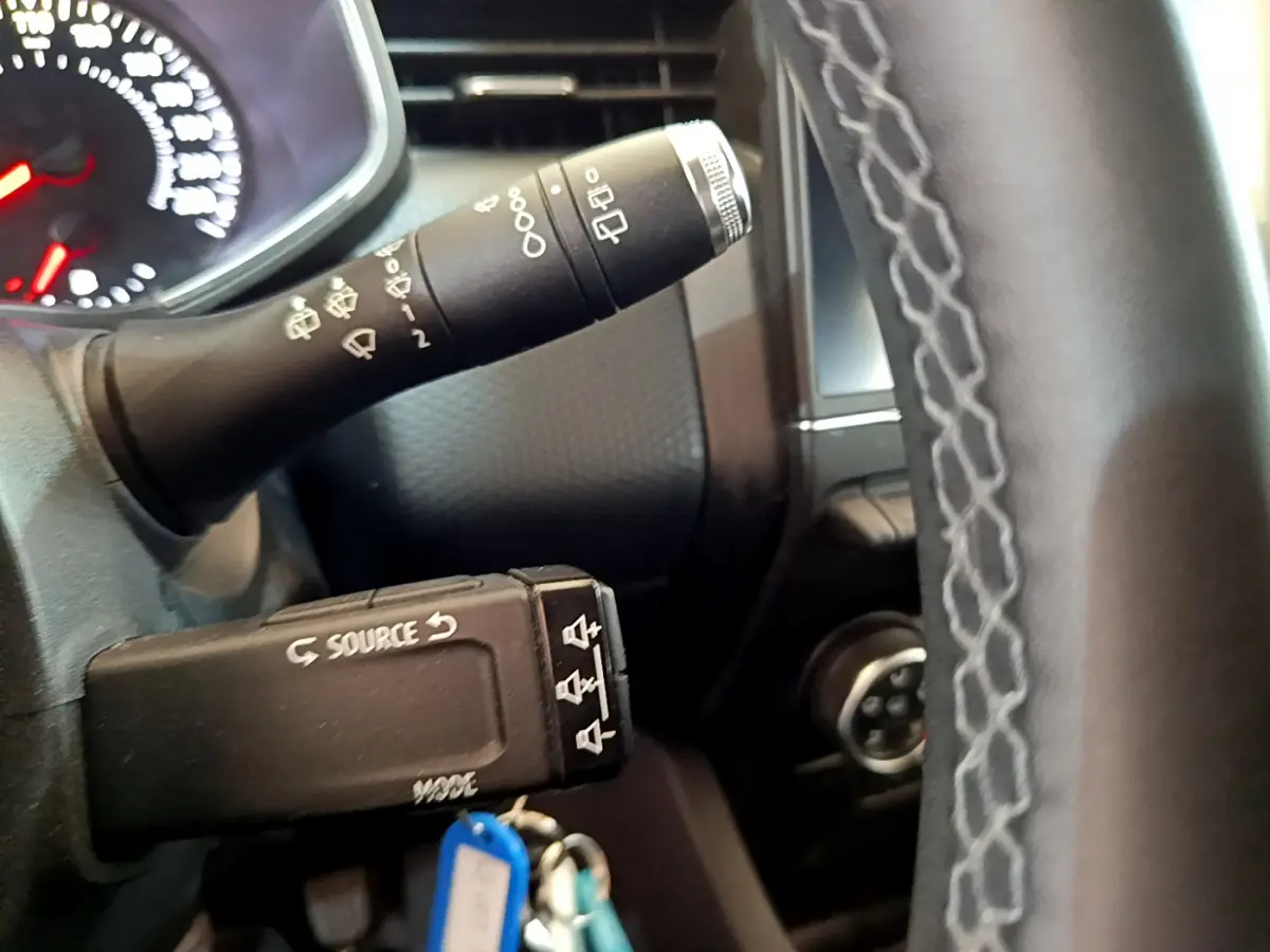 Gros plan sur la manette de commandes au volant et le volant en cuir synthétique de la Renault Clio blanche 2020.