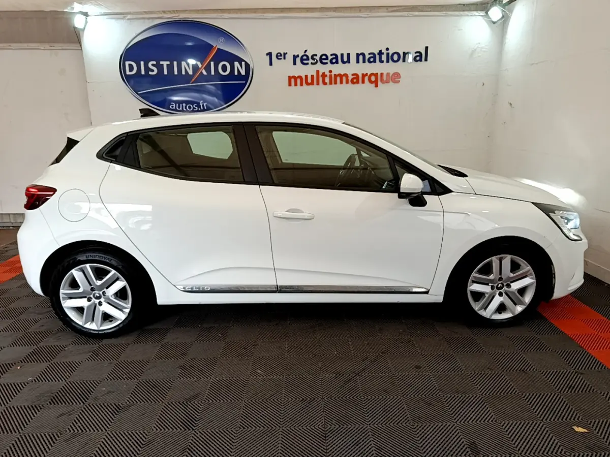 Profil droit d'une Renault Clio Business Blue dCi 85 blanche, avec jantes alliage et rétroviseurs blancs dans un showroom.