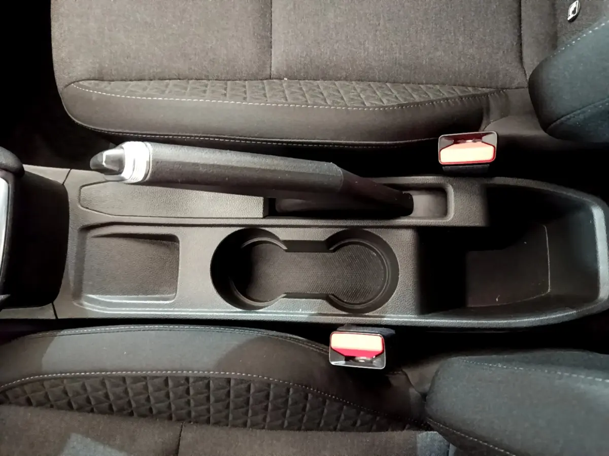 Vue plongeante sur la console centrale noire de la Renault Clio Business Blue dCi 85 avec frein à main et porte-gobelets.