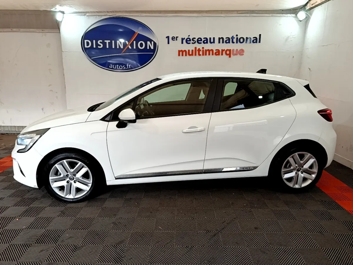 Profil droit d’une Renault Clio Business Blue dCi 85 blanche, avec jantes alliage et feux arrière LED visibles en intérieur showroom.