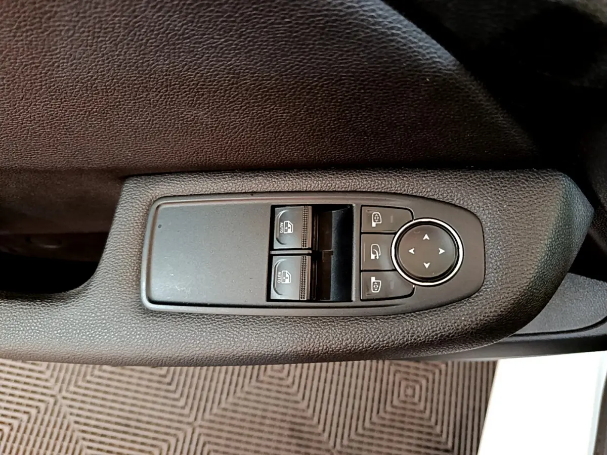 Gros plan sur les commandes de lève-vitres et rétroviseurs sur la porte côté conducteur d’une Renault Clio blanche.