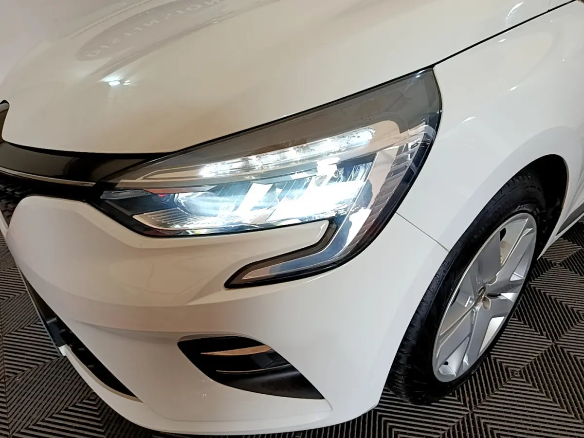 Gros plan sur l'avant droit blanc d'une Renault Clio 2020 avec phares LED allumés et jante alliage visible.