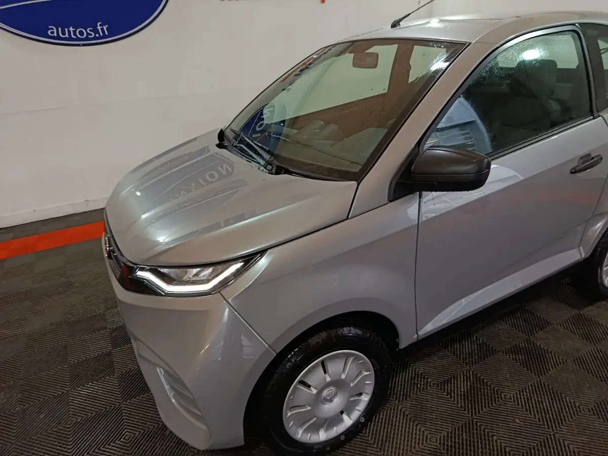 Vue 3/4 avant droit d'une Aixam Ambition 0.5 City Pack gris clair avec rétroviseur caméra côté conducteur.