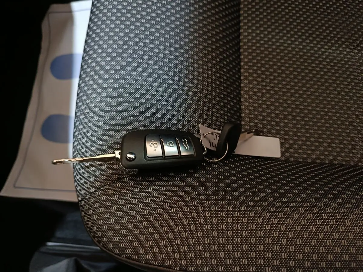 Clé de voiture AIXAM AMBITION 0.5 CITY PACK posée sur un siège tissu gris à motifs, vue rapprochée intérieure.