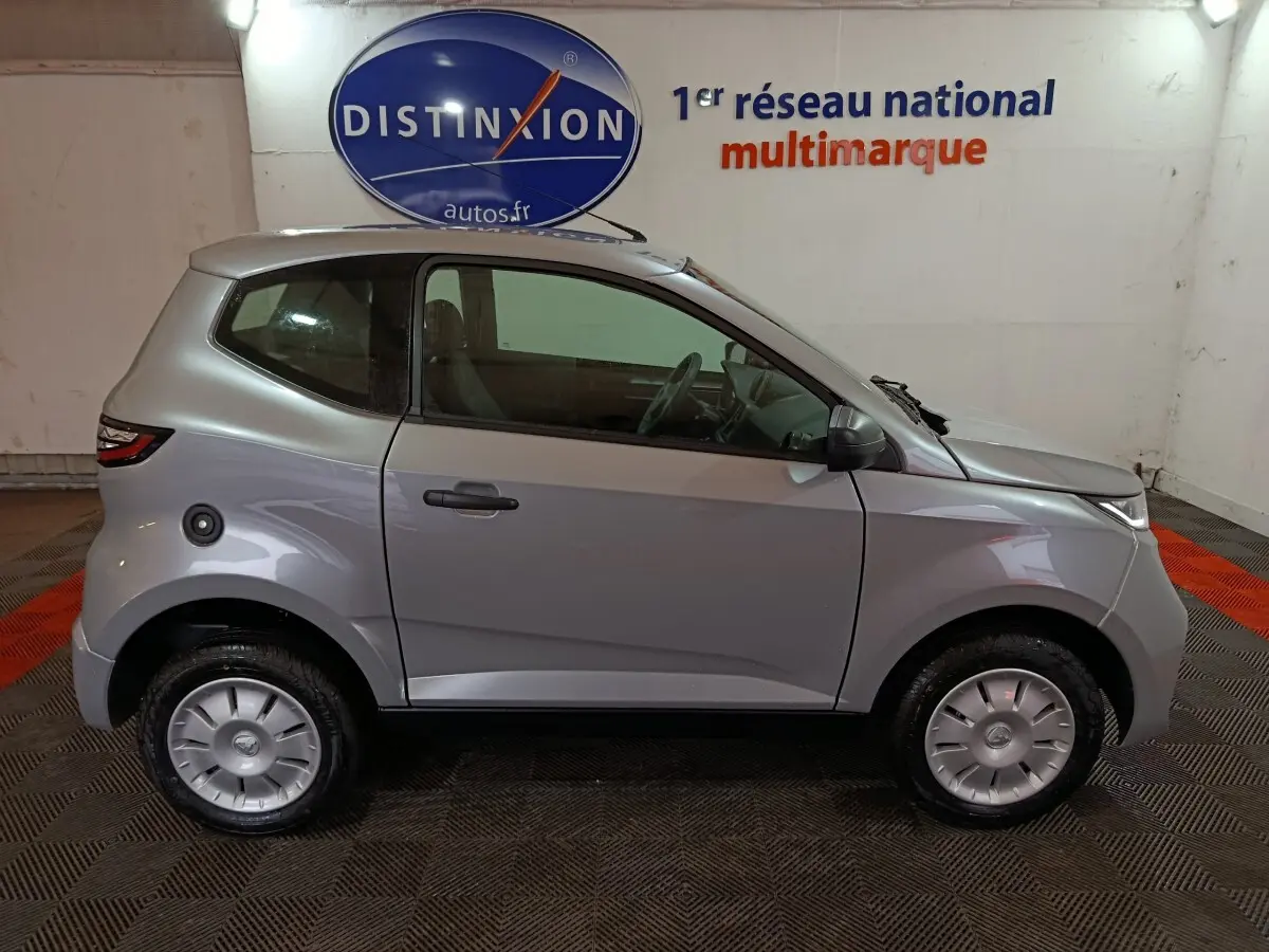 Vue de profil côté gauche d'une Aixam Ambition 0.5 City Pack gris clair 2026 avec rétroviseur caméra côté conducteur.