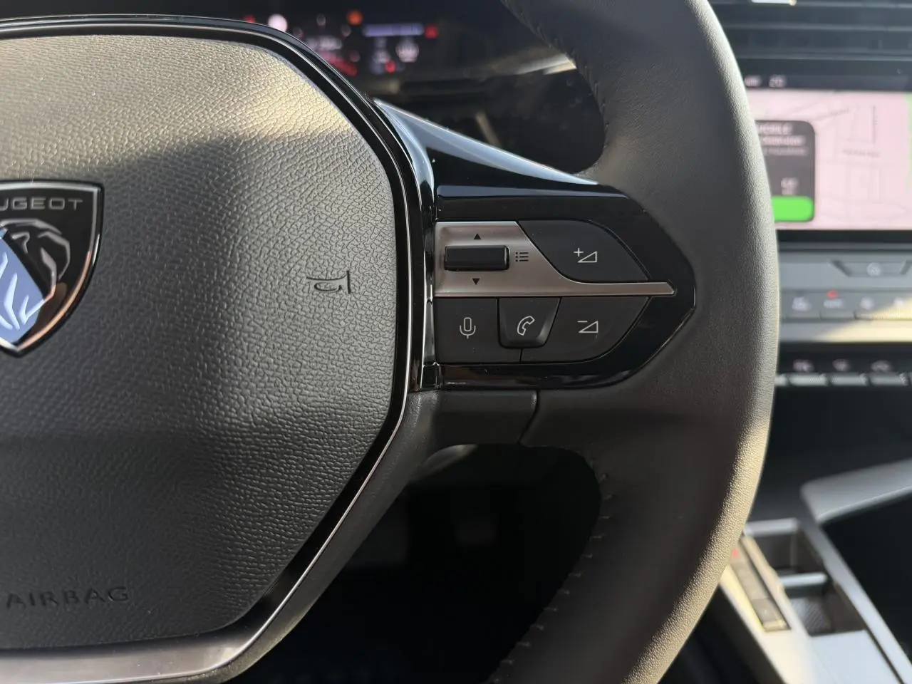 Gros plan sur le volant cuir noir de la Peugeot 308 2025, avec commandes multimédia et logo Peugeot visible.