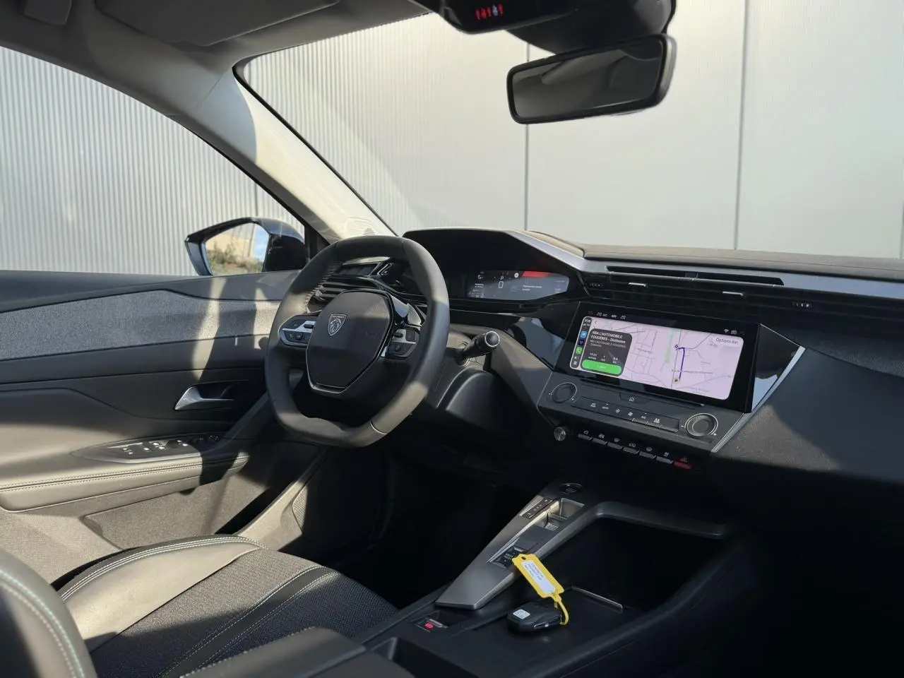 Vue intérieure côté conducteur de la Peugeot 308 2025, volant cuir, écran tactile 10 pouces avec navigation affichée.