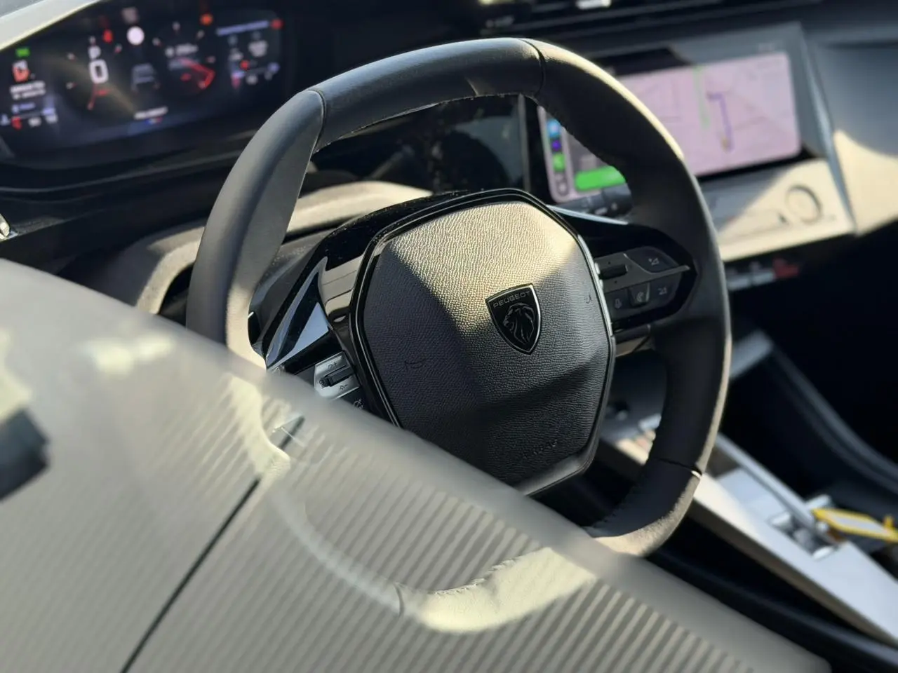 Vue rapprochée du volant cuir noir de la Peugeot 308 2025 avec tableau de bord numérique et écran tactile visible.