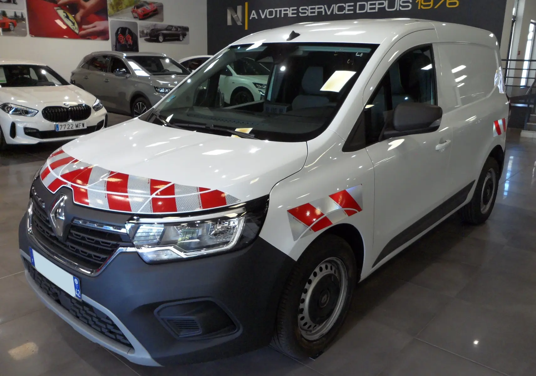 Vue 3/4 avant droit d'un Renault Kangoo Van blanc minéral avec marquages réfléchissants rouges et argentés sur le capot et l'aile.