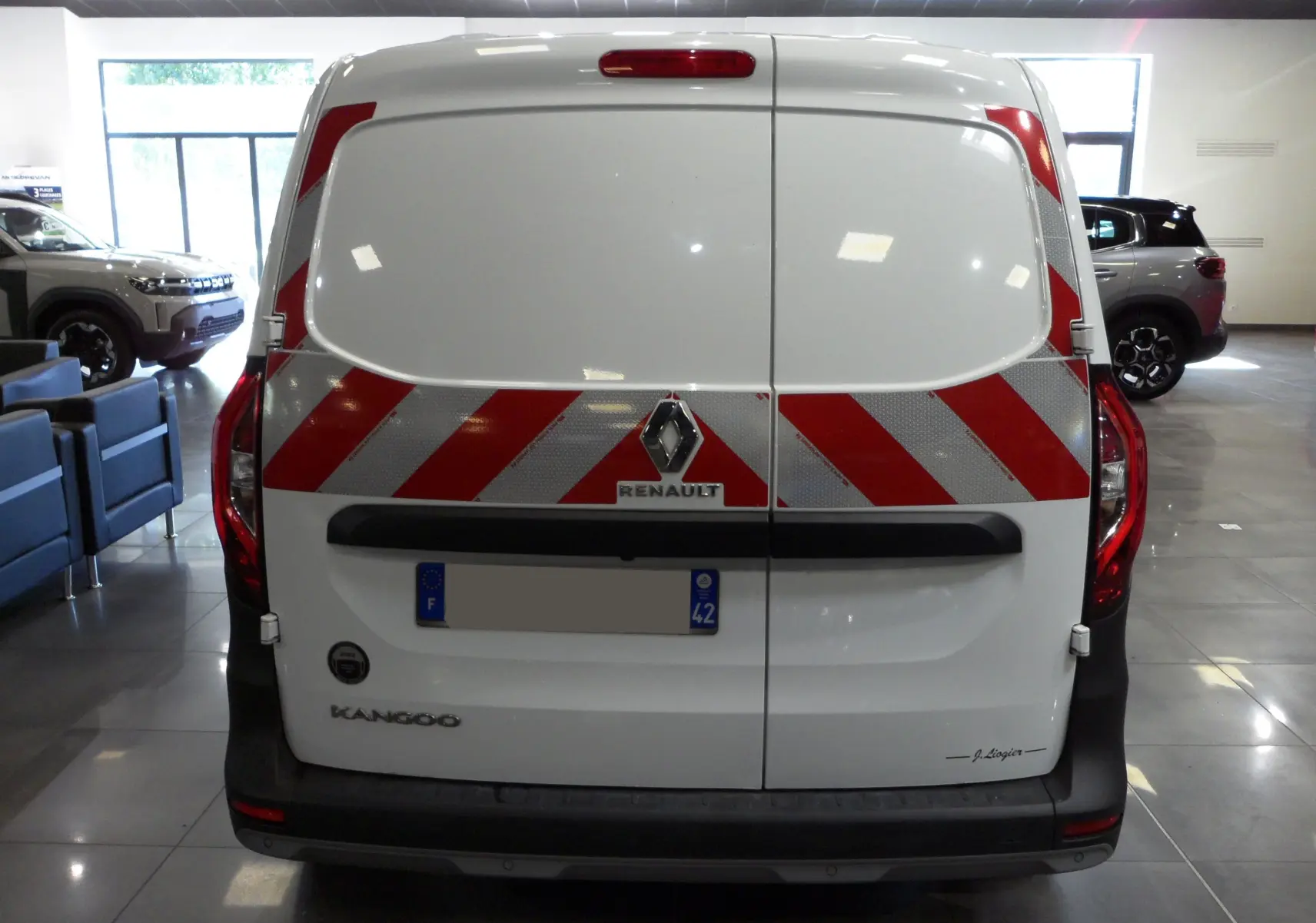 Vue arrière d'un Renault Kangoo Van blanc minéral avec bandes réfléchissantes rouges et grises en diagonale.