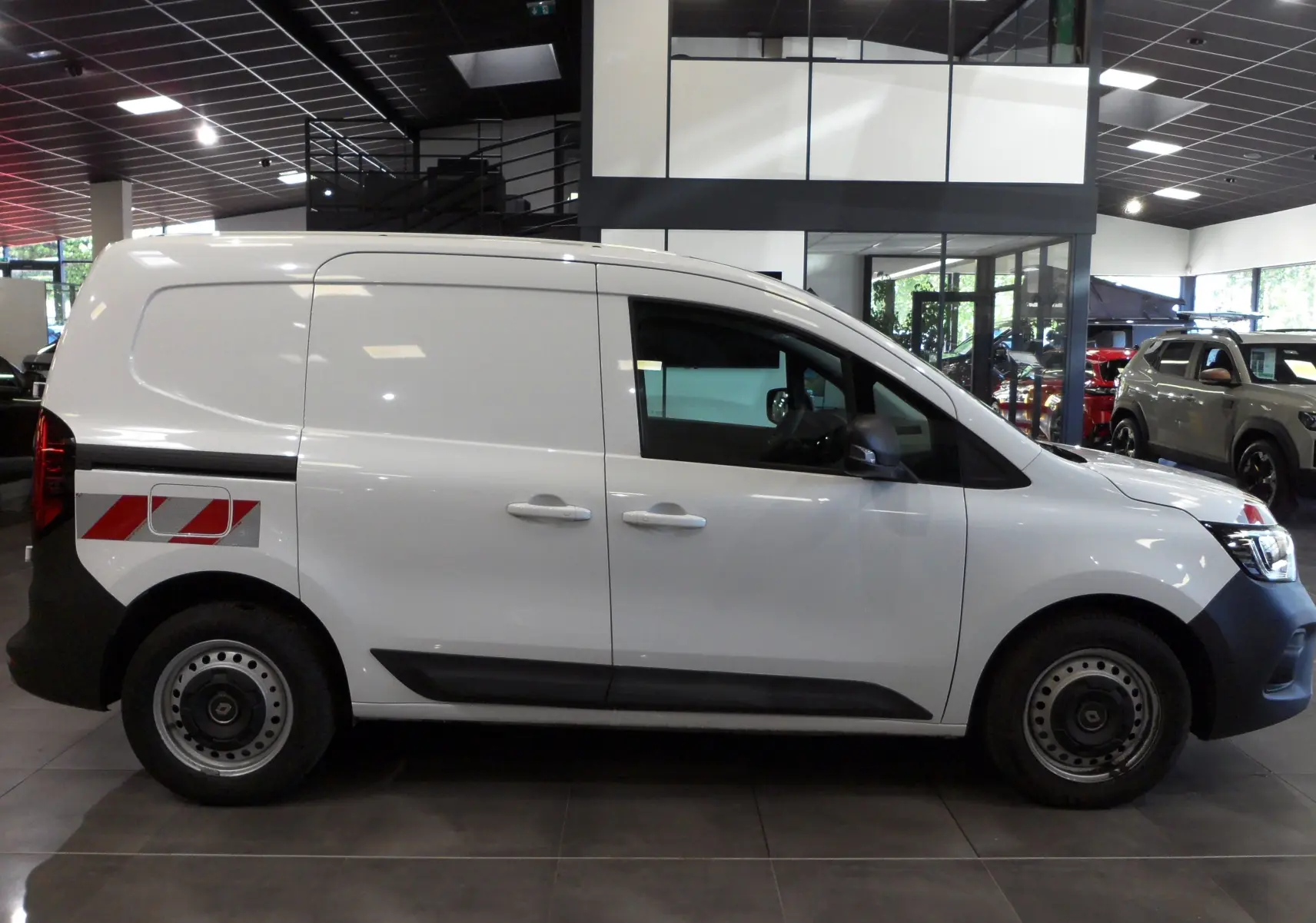 Profil droit du Renault Kangoo Van blanc minéral 2022 avec marquage rouge et blanc sur l'aile arrière dans un showroom.