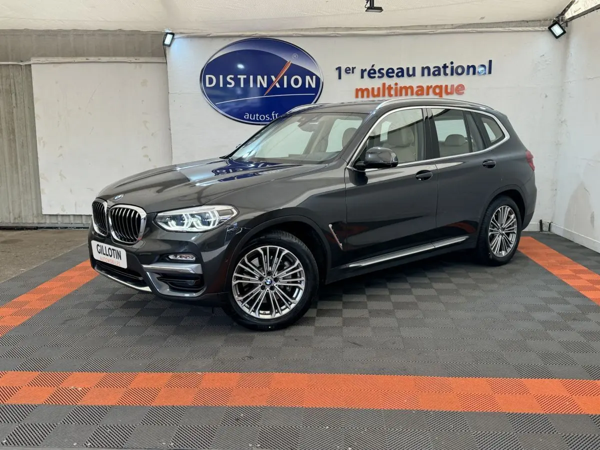 BMW X3 xDrive30d gris foncé vu de 3/4 avant droit dans un showroom avec sol noir et orange.