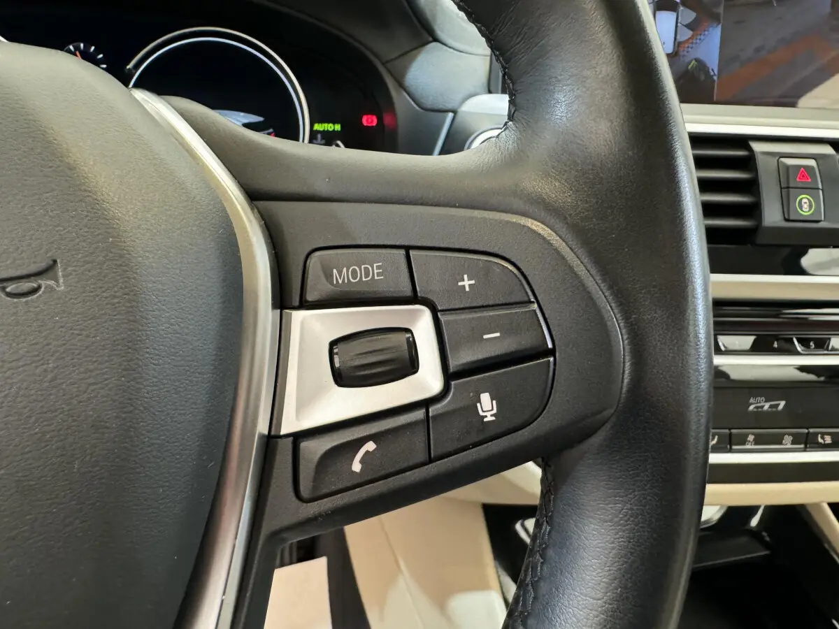 Gros plan sur le côté gauche du volant en cuir noir d'une BMW X3 gris foncé, avec commandes audio et vocales intégrées.