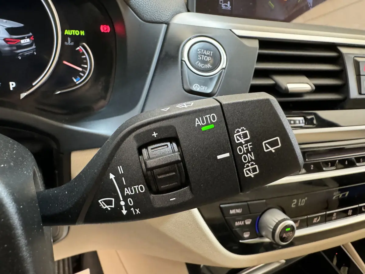 Gros plan sur la commande d’essuie-glace avec bouton start-stop, tableau de bord beige et noir d’un BMW X3 gris foncé.