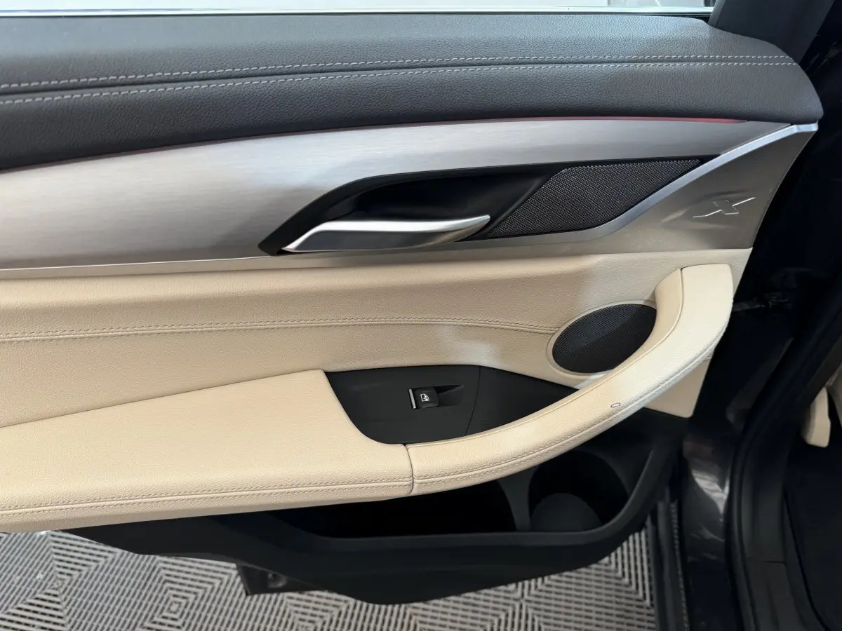 Gros plan sur la porte côté gauche d'une BMW X3 gris foncé, avec garniture beige et insert aluminium marqué "X".