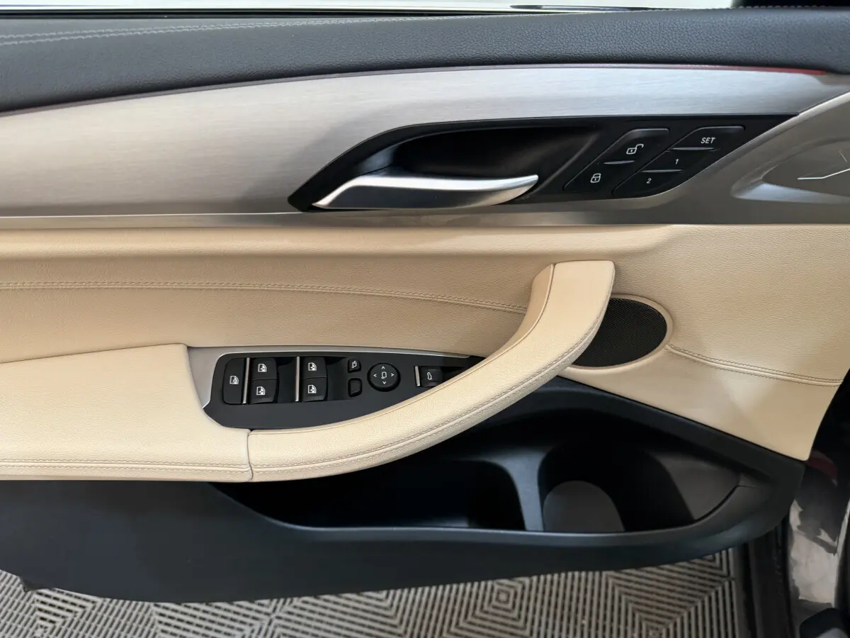 Poignée de porte côté gauche beige et noir de BMW X3 2018 avec commandes de vitres et verrouillage intégrées.