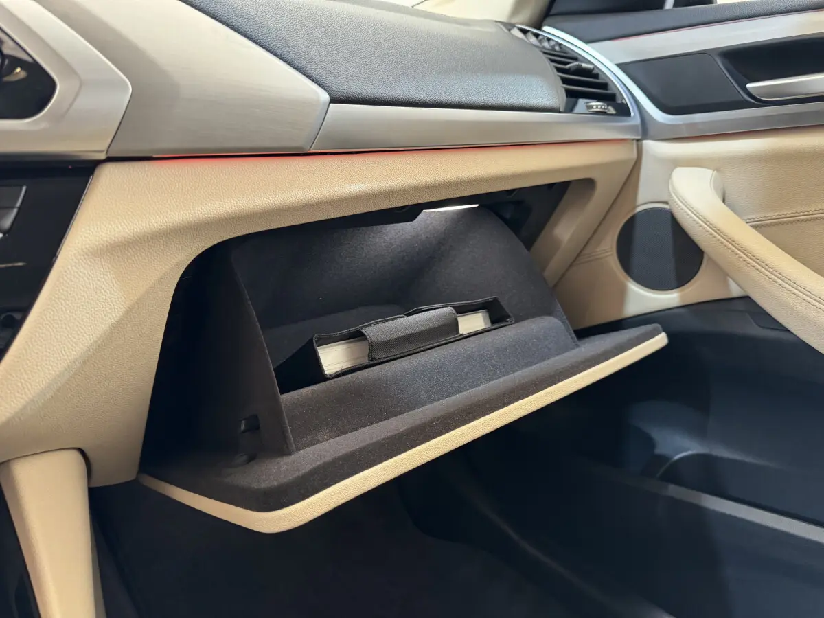 Intérieur beige du BMW X3 xDrive30d 2018, vue côté passager sur la boîte à gants ouverte avec manuel visible.