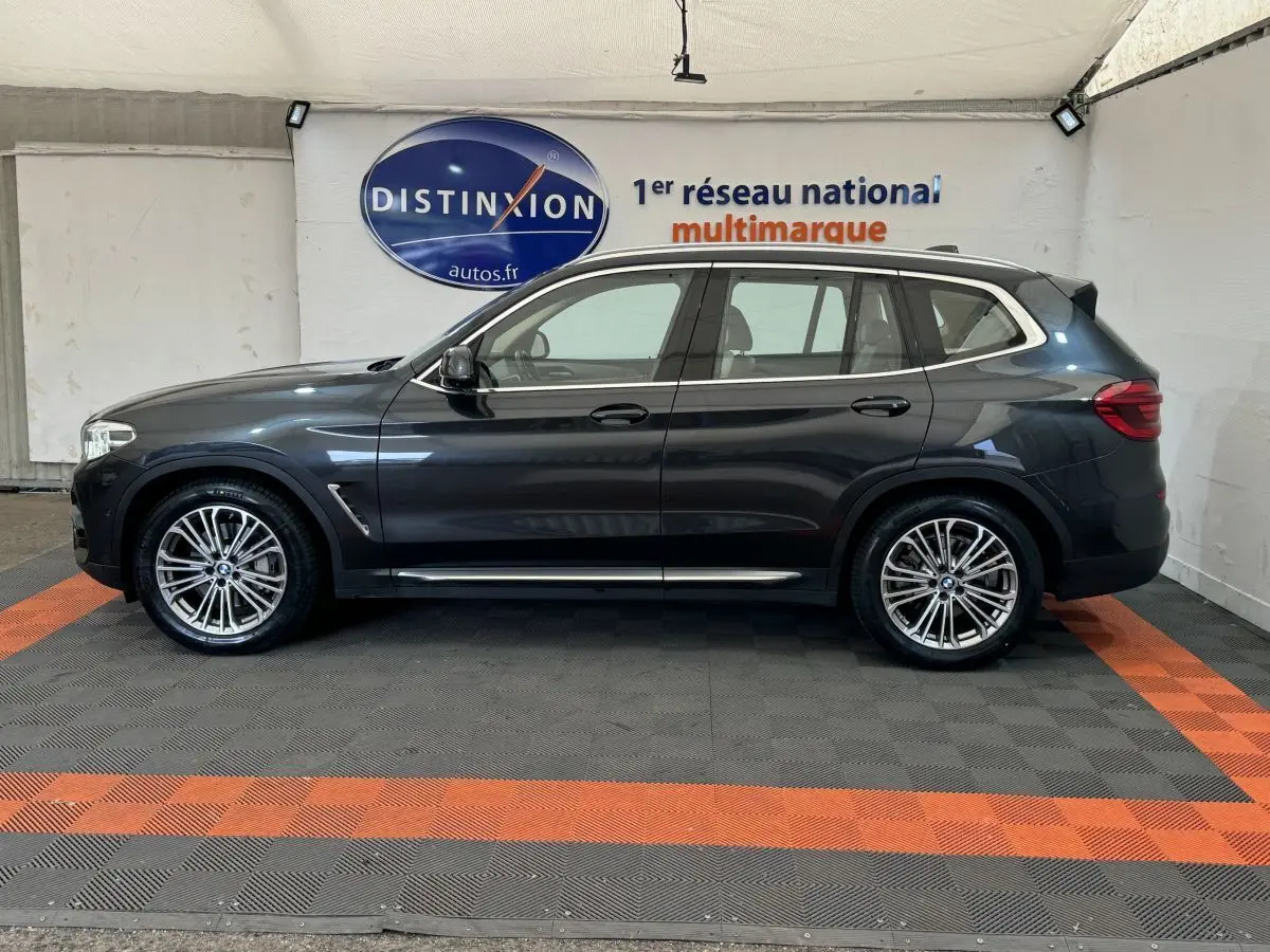 Profil droit d'un BMW X3 gris foncé 2018 Luxury avec jantes alliage et rails de toit chromés en intérieur showroom.