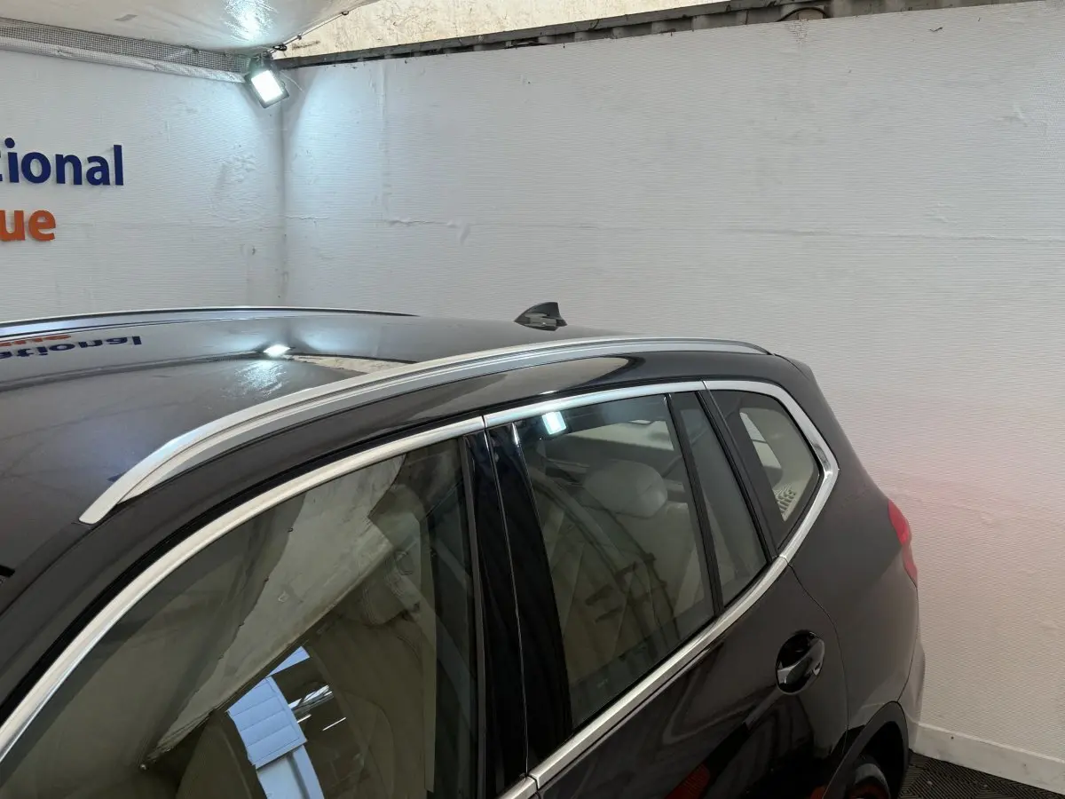 Vue latérale arrière droite d'un BMW X3 gris foncé avec barres de toit chromées dans un garage.