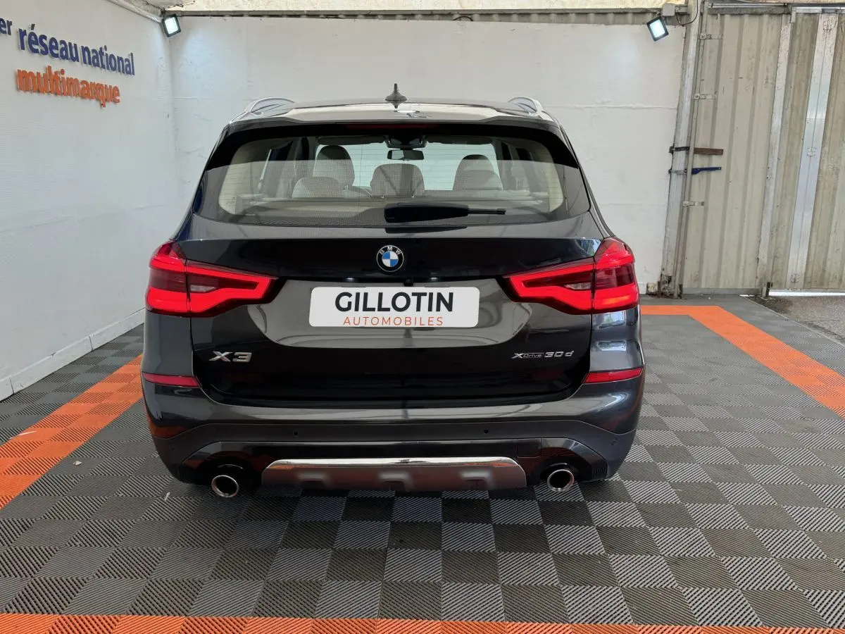 Vue arrière d'un BMW X3 xDrive30d gris foncé avec feux LED allumés et double sortie d'échappement visible.
