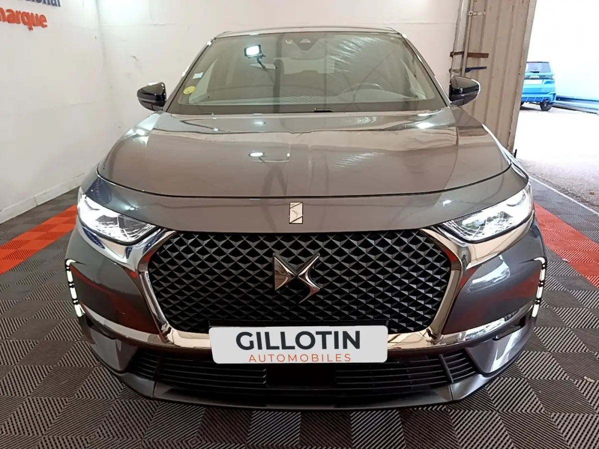 Vue frontale d'un DS7 Crossback gris foncé avec calandre noire à motif losange et phares LED allumés.
