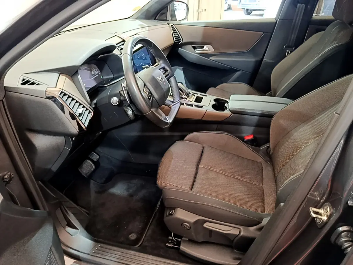 Vue intérieure côté conducteur du DS7 Crossback gris foncé, montrant le volant cuir, tableau de bord digital et sièges tissu foncé.