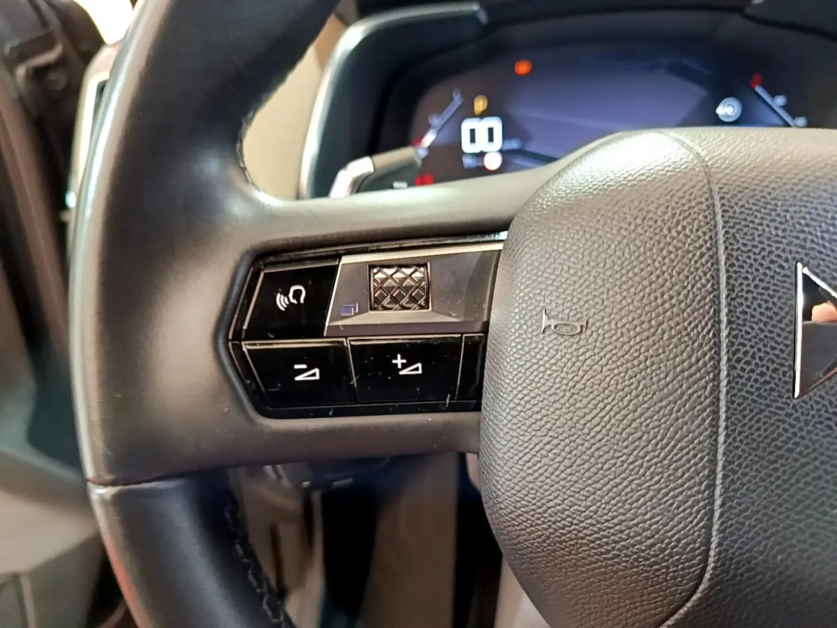 Gros plan sur le volant cuir noir du DS7 Crossback 2020, avec commandes intégrées et tableau de bord numérique en arrière-plan.