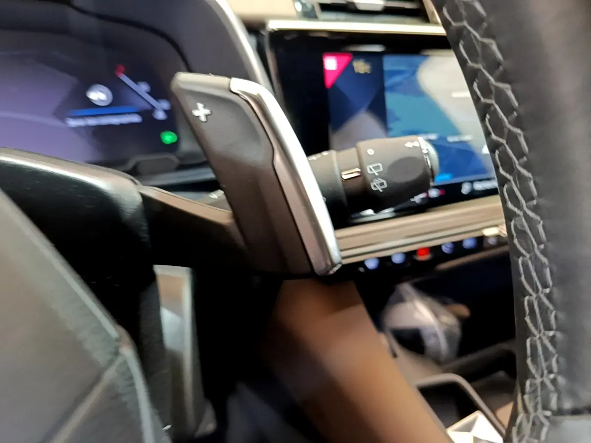 Gros plan sur la palette de changement de vitesse côté droit du volant cuir du DS7 Crossback gris foncé, avec écran tactile en arrière-plan.