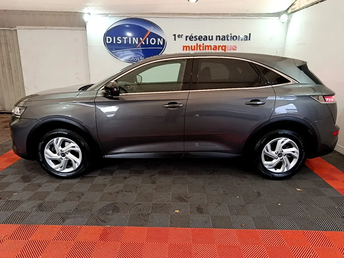 Vue de profil côté gauche d'un DS7 Crossback gris foncé garé en intérieur avec jantes alliage et vitres teintées.