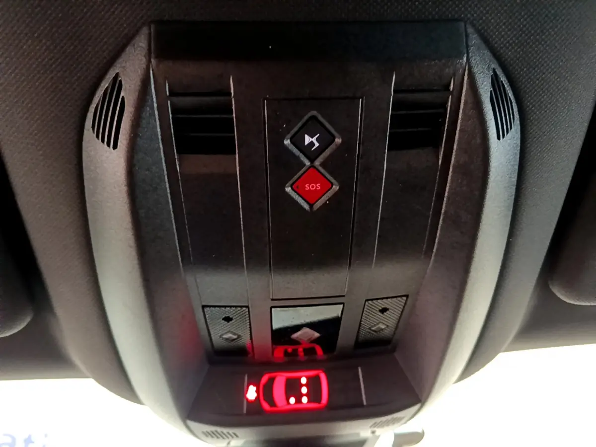Vue en contre-plongée du panneau de commandes au plafond du DS7 Crossback gris foncé, avec bouton SOS rouge et éclairage rouge d'alerte.