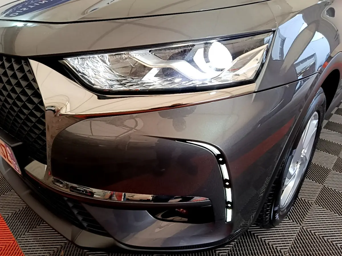 Gros plan sur le phare avant droit allumé du DS7 Crossback gris foncé, mettant en valeur la calandre et les feux LED distinctifs.