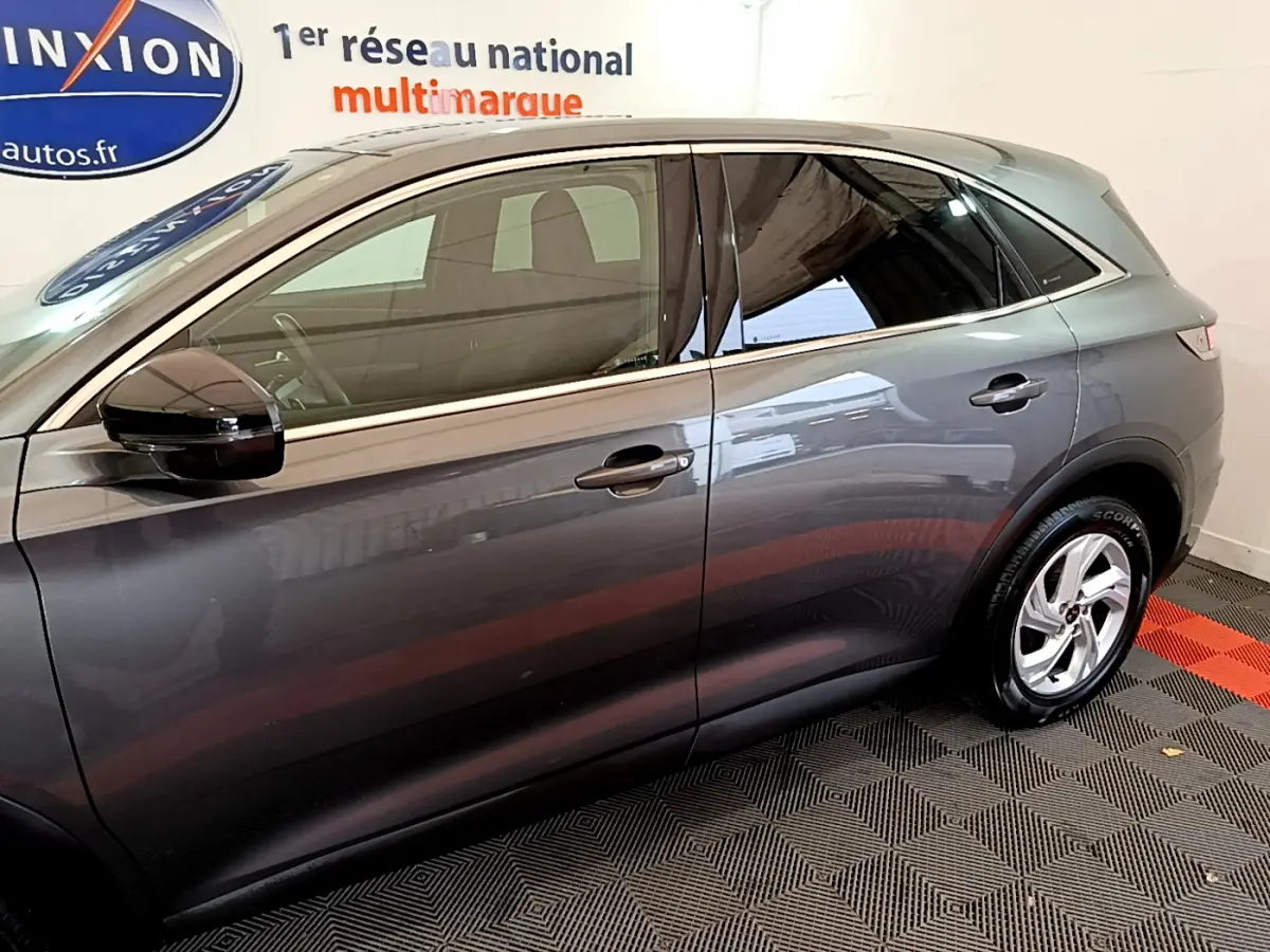 Vue latérale côté gauche d’un DS7 Crossback gris foncé garé en intérieur sur sol à motifs rouges et noirs.