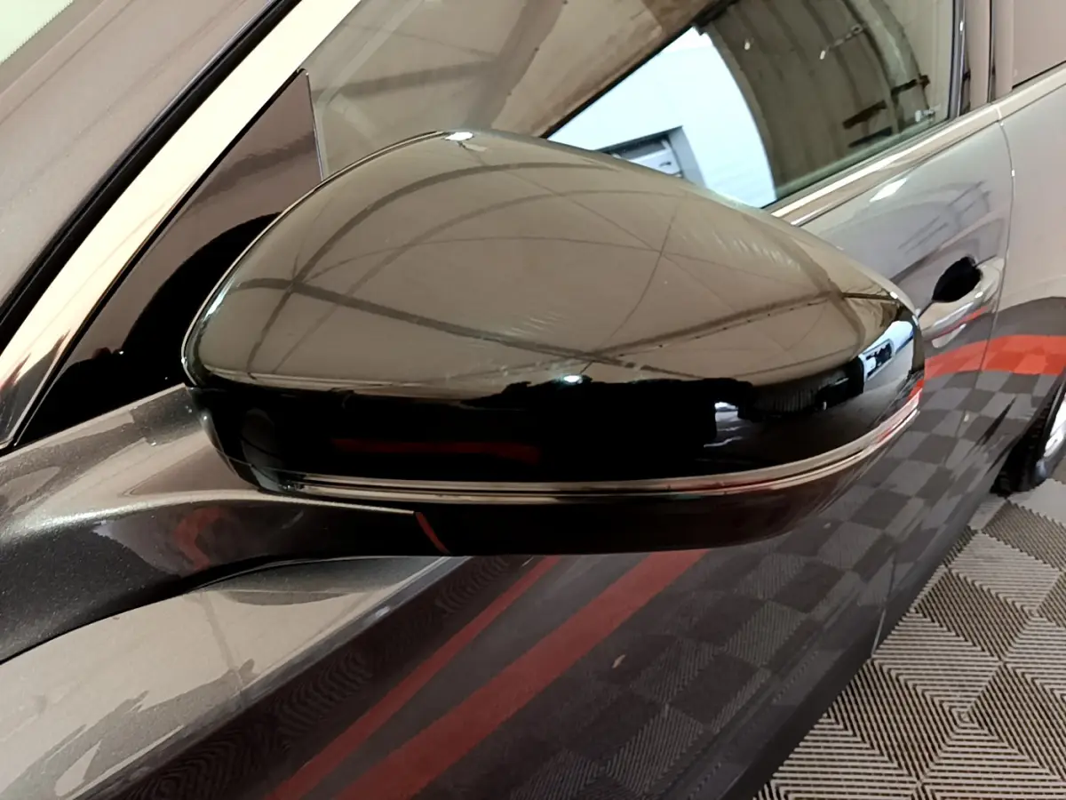 Rétroviseur droit noir brillant du DS7 Crossback gris foncé, vue rapprochée avec reflet de l'environnement intérieur.