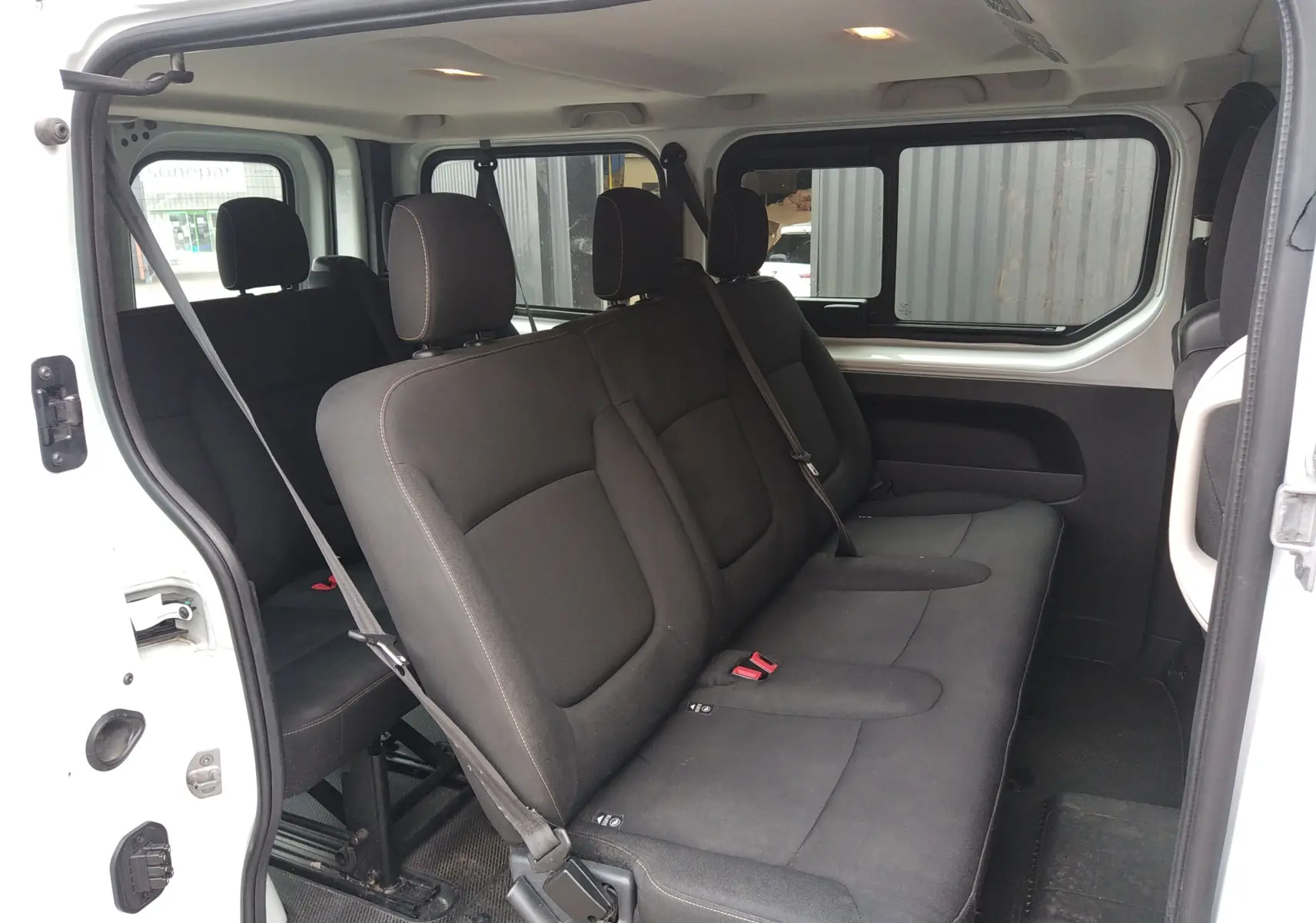 Vue intérieure côté droit du Renault Trafic Microbus blanc, montrant les sièges tissu noirs sur trois rangées.