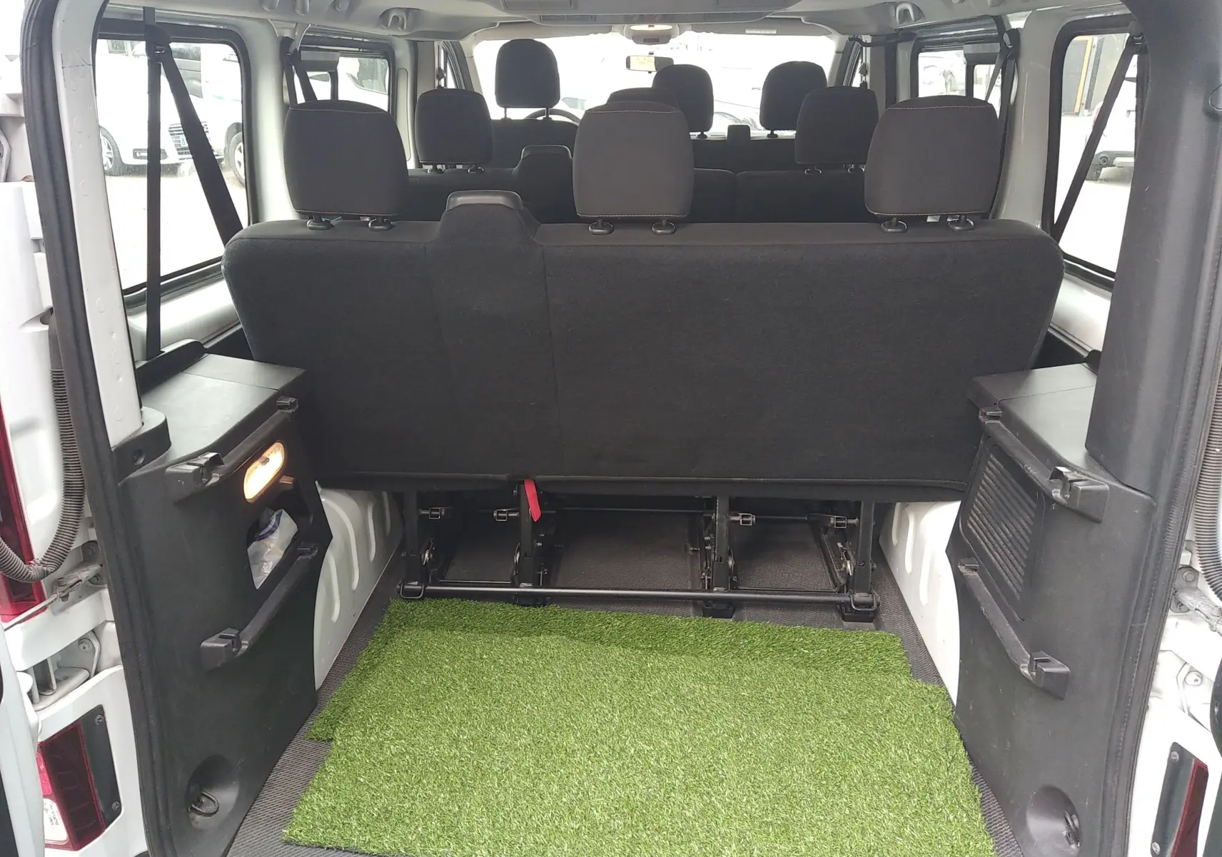 Vue arrière ouverte du Renault Trafic Microbus blanc montrant l'espace de chargement avec tapis vert et sièges arrière en tissu noir.