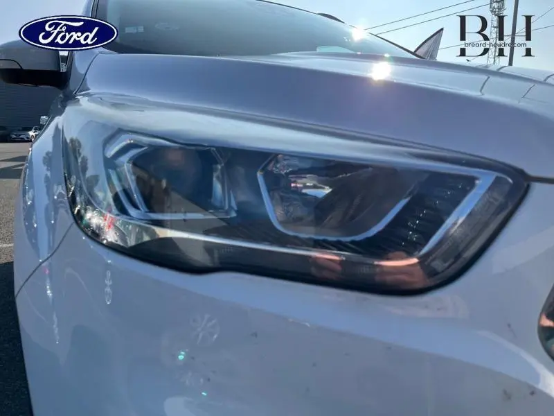 Gros plan sur le phare avant droit du Ford Kuga blanc Glacier, mettant en valeur son design moderne et anguleux.