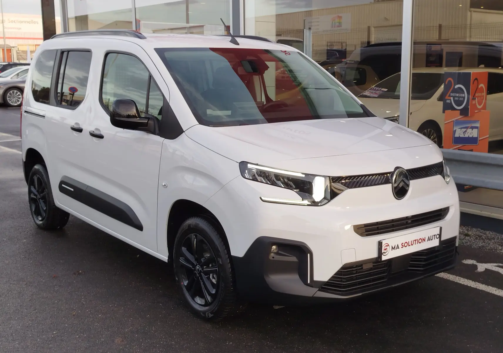 Vue 3/4 avant droite d'un Citroën Berlingo Kaolin White avec jantes noires et protections latérales noires.