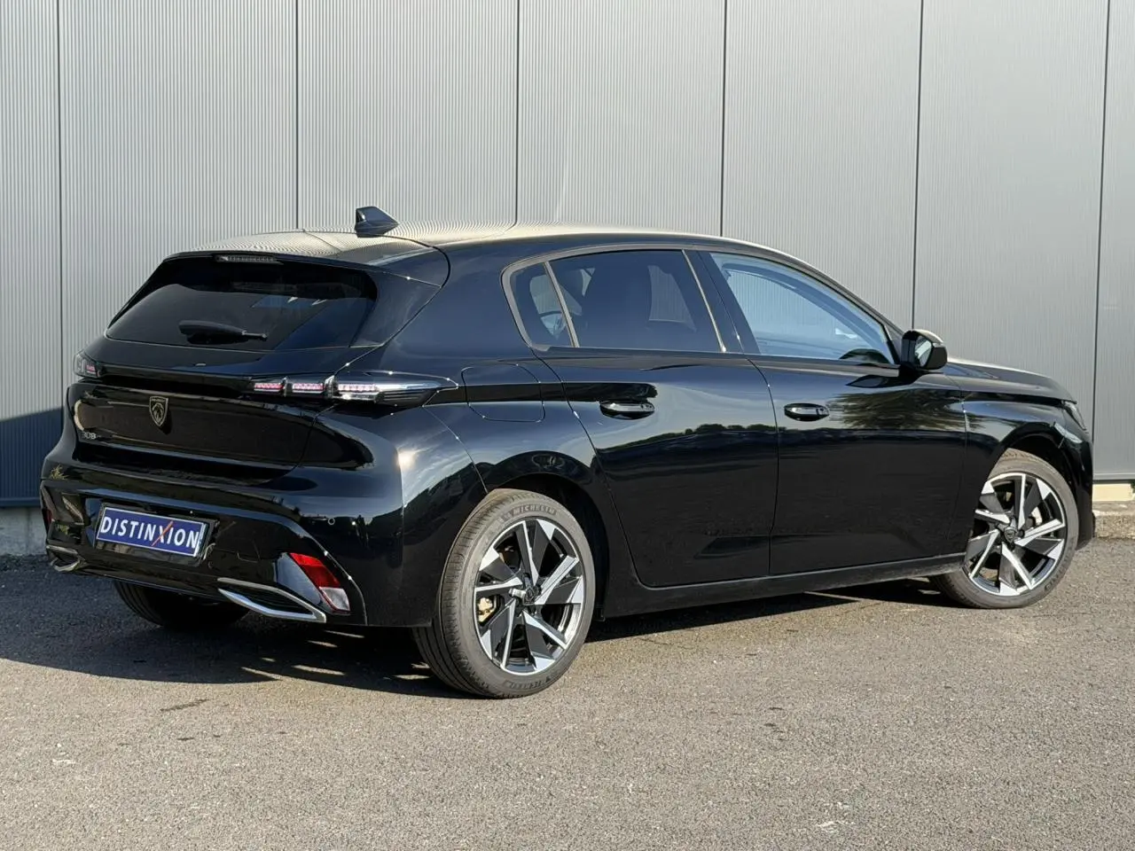 Vue 3/4 arrière droite d'une Peugeot 308 noire Perla avec jantes alliage 17 pouces et bandeau noir brillant arrière.