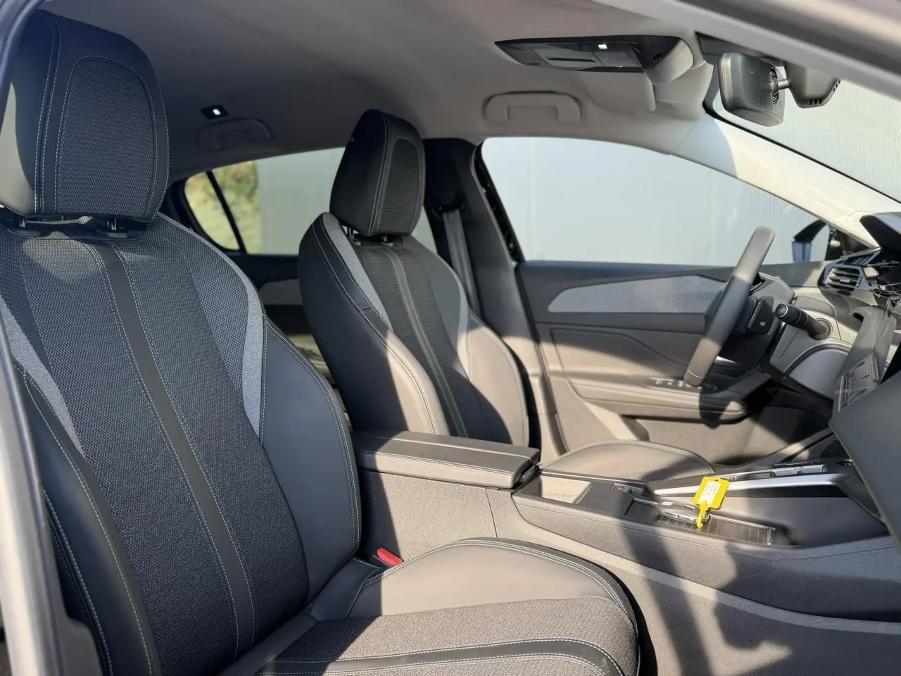 Intérieur de la Peugeot 308 2025 vu côté conducteur, sièges tissu et cuir gris avec accoudoir central.