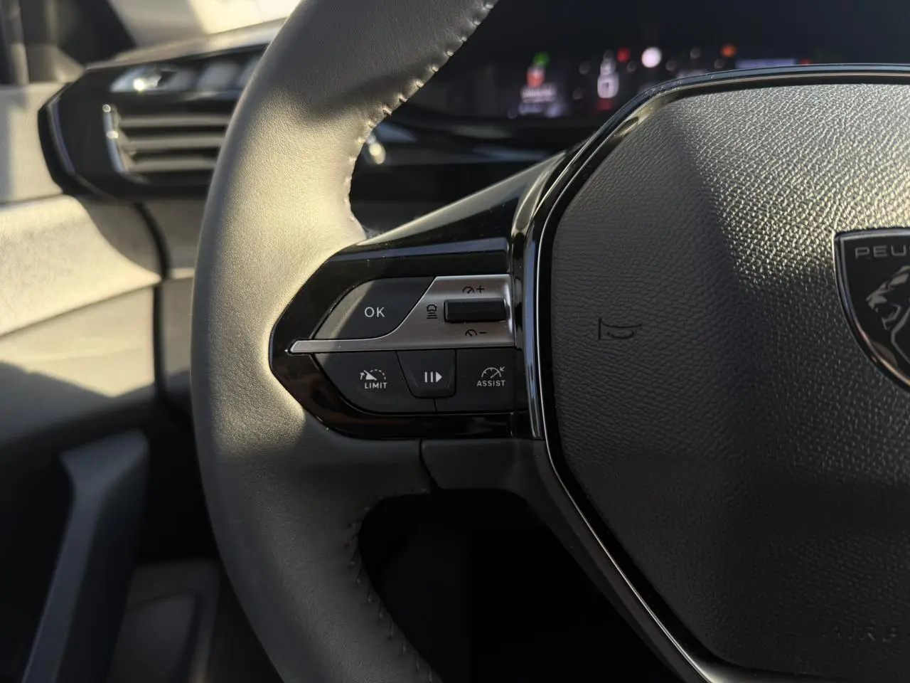 Gros plan sur le volant cuir noir de la Peugeot 308 2025, avec commandes intégrées et logo central visible.