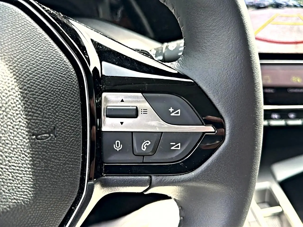 Gros plan sur le côté gauche du volant cuir noir d'une Peugeot 408 Hybrid 136 allure 2024 avec commandes vocales et téléphone.