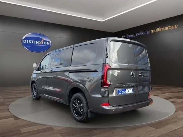 Vue 3/4 arrière droite d’un Volkswagen Transporter gris foncé avec jantes noires, dans un showroom intérieur.