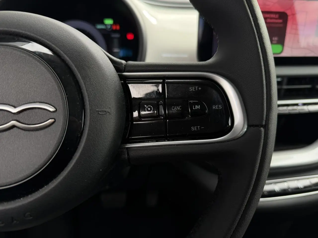 Gros plan sur le volant noir Soft-Touch de la Fiat 500 électrique 2024 avec commandes de régulateur de vitesse.